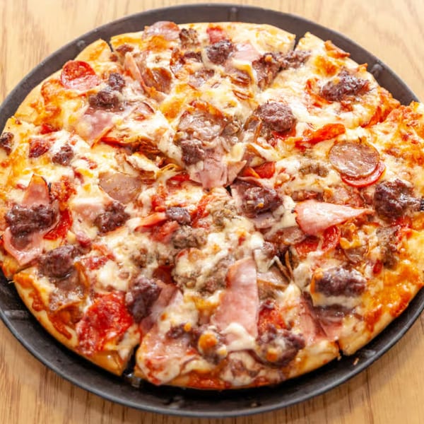 Antigoni's Pizza with pepperoni, ham, and sausage on a black pan.