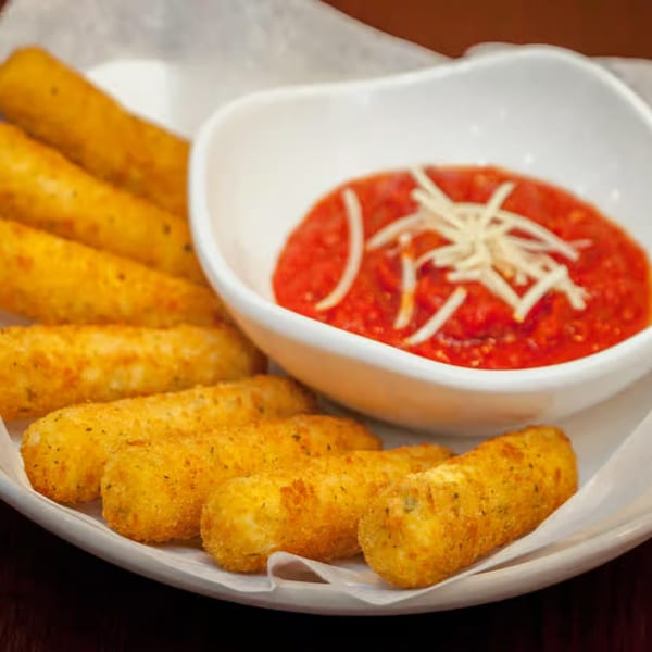 Golden-brown mozzarella sticks with a side of marinara sauce topped with shredded cheese.