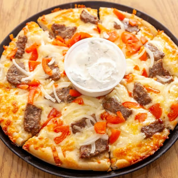 Antigoni's Pizza with beef, onions, and tomatoes, served with a side of white sauce.