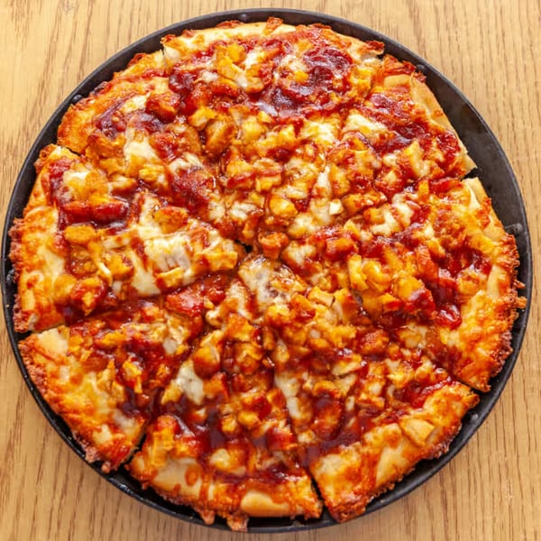 Antigoni's Pizza BBQ chicken pizza, sliced and served in a black pan on a wooden table.